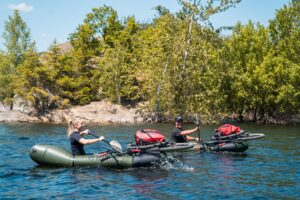 A packrafter paddling through a scenic river in the Eifel, surrounded by lush forests.